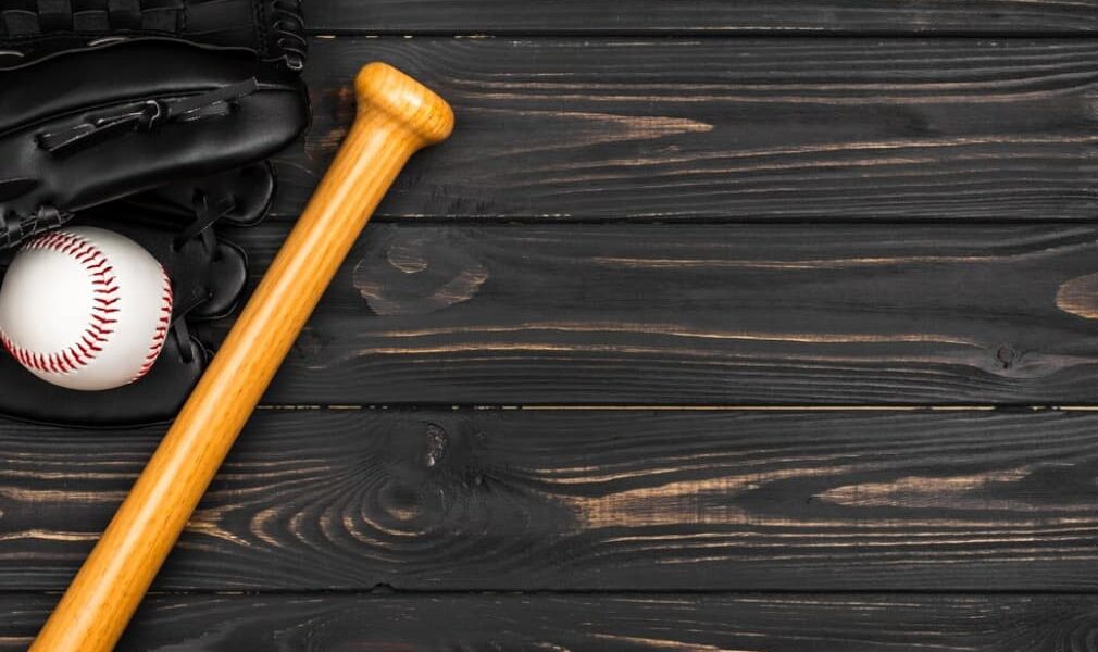 Baseball bat, glove, and ball on dark wooden background